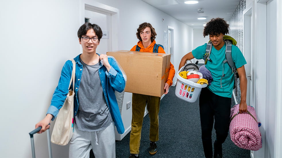A wide-angle view of a group of three male students who are also friends moving into their new student accommodation